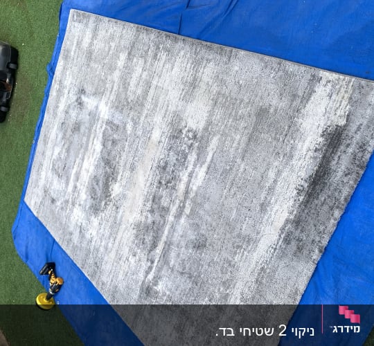 שטיח אפור על יריעת פלסטיק כחולה עם מכונת ניקוי
